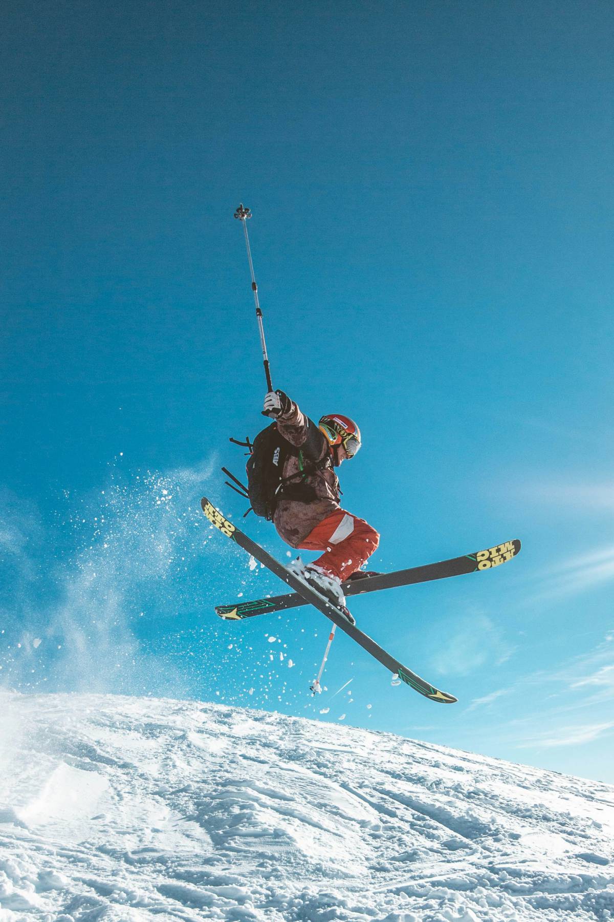 Skifahrer springt mit gekreuzten Skiern vor blauem Himmel in die Luft