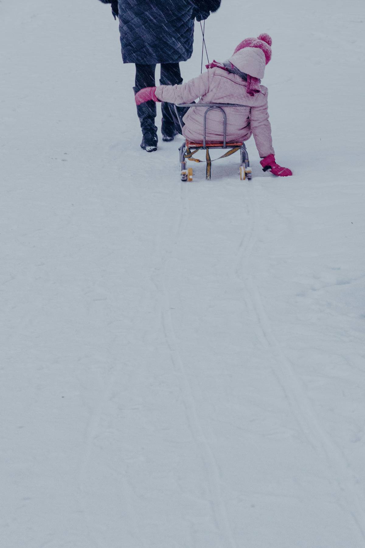 Frau zieht Kind in rosa Kleidung auf einem Schlitten durch den Schnee