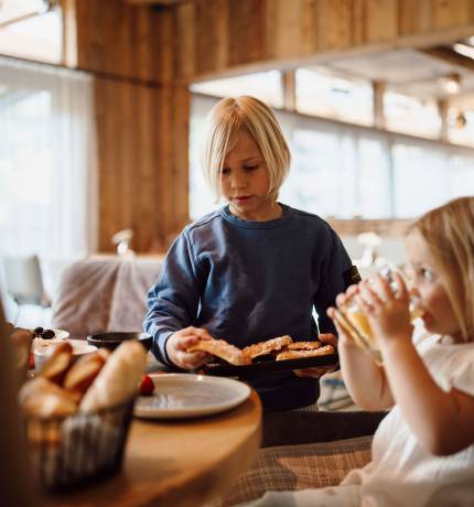 Junge und Mädchen essen und trinken am Tisch im Restaurant Glückskind Ferienresort Central Flachau