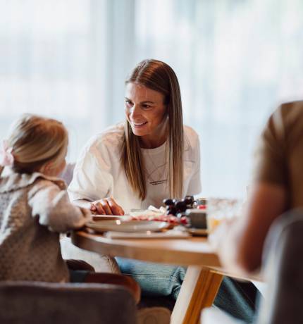 Lächelnde Frau und Kind sitzen am gedeckten Tisch im Restaurant Glückskind Ferienresort Central Flachau