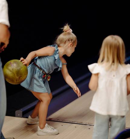 Mädchen in blauem Kleid spielt Bowling mit Familie