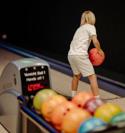 Kind mit orangener Bowlingkugel auf der Bowlingbahn