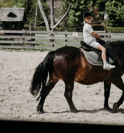 Kind reitet auf braunem Pferd im Ferienresort Central Flachau