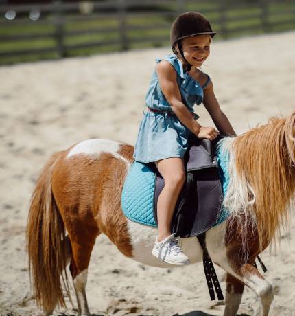 Lachendes Mädchen reitet auf Miniaturpferd im Ferienresort Central Flachau