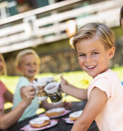 Fröhliche Familie bei der Jause mit Krapfen auf einer Alm