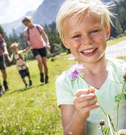 Lachendes Kind mit Blume und Familie im Hintergrund