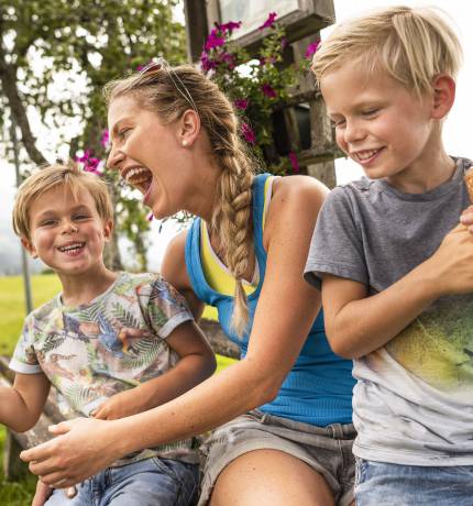 Mutter und zwei Kinder beim Eis essen auf einer Bank im Grünen