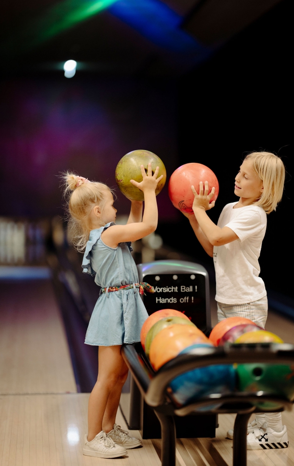 Zwei Kinder mit bunten Bowlingkugeln auf der Bowlingbahn