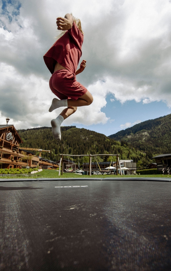 Kind in roter Kleidung springt auf Trampolin im Ferienresort Central Flachau