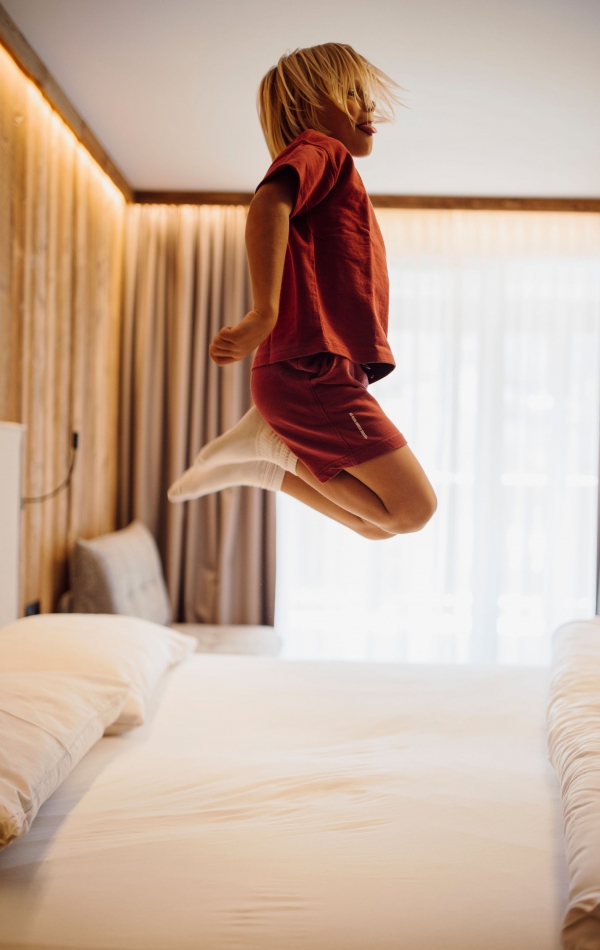 Blonder Junge mit roter Kleidung springt auf einem Bett in die Luft