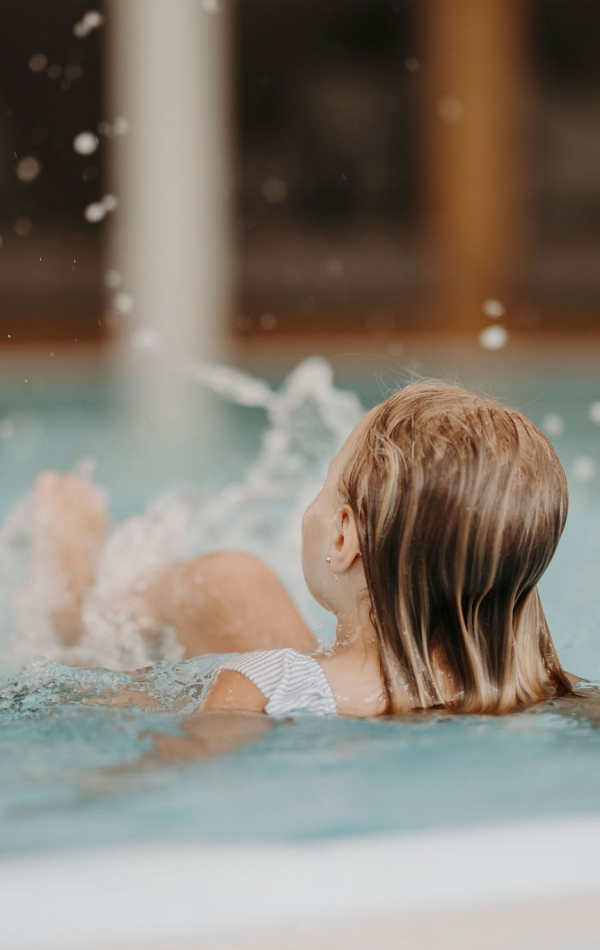 Kind von hinten plantscht mit Füßen im Wasser