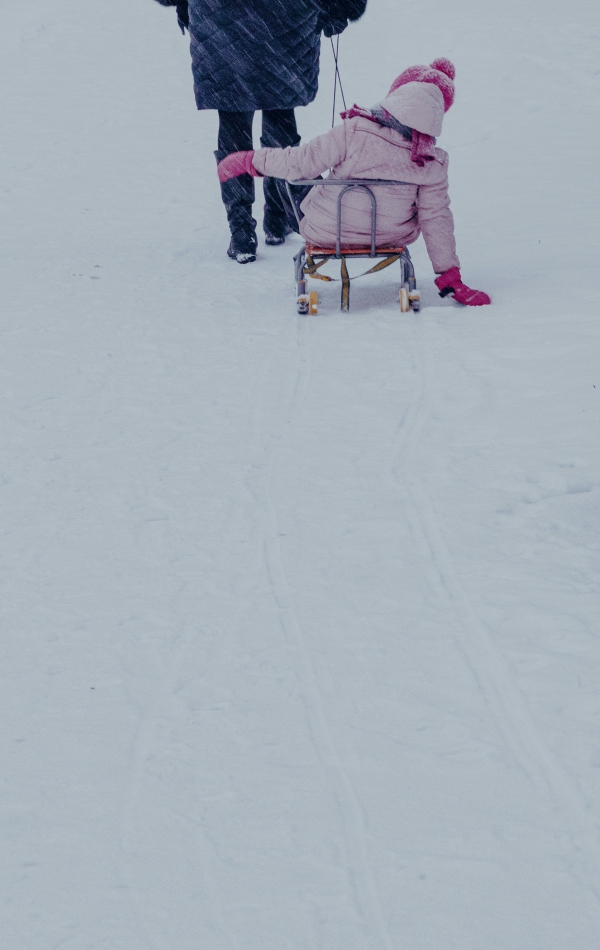 Frau zieht Kind in rosa Kleidung auf einem Schlitten durch den Schnee