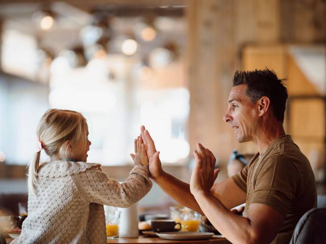 Vater und Tochter mit High Five am Frühstückstisch