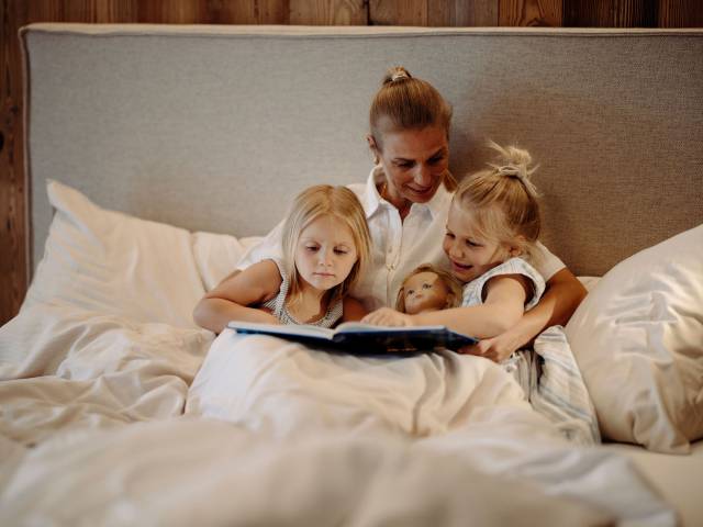 Mutter und zwei Kinder liegen mit einem Buch im Bett