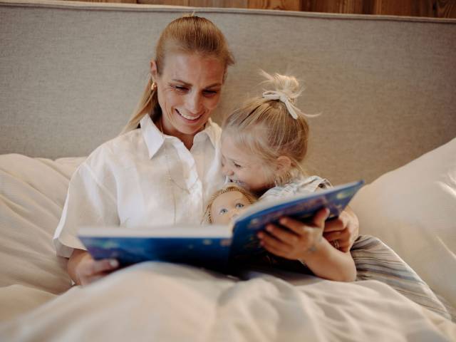 Mutter und Tochter mit Puppe lesen ein Buch im Bett