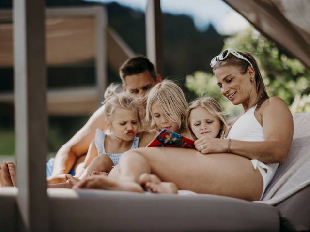 Familie auf Sonnenliege liest gemeinsam ein Buch