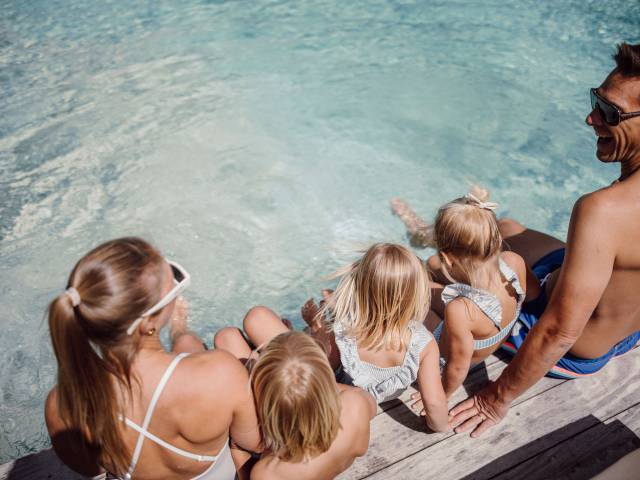 Familie in Badesachen sitzt am Pool im Ferienresort Central Flachau