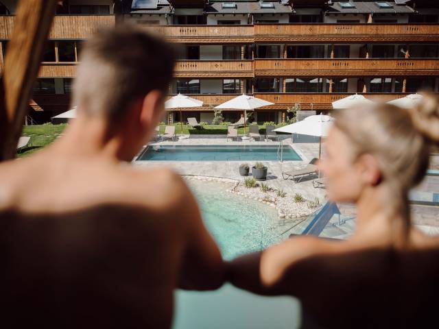 Paar blickt vom Balkon auf den Außenpool im Ferienresort Central Flachau