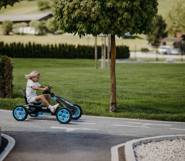 Blondes Kind fährt mit blau-schwarzem Go Kart den Berg hinunter