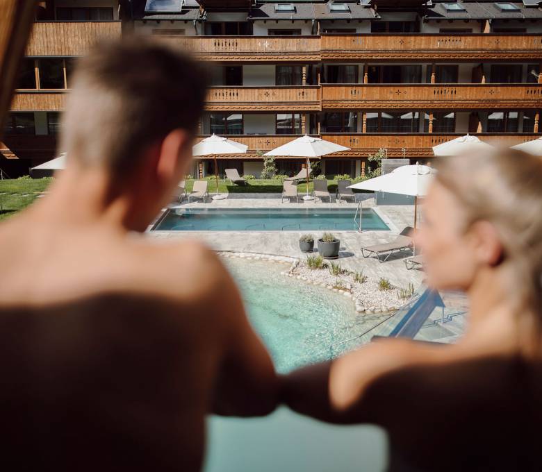 Paar blickt vom Balkon auf den Außenpool im Ferienresort Central Flachau